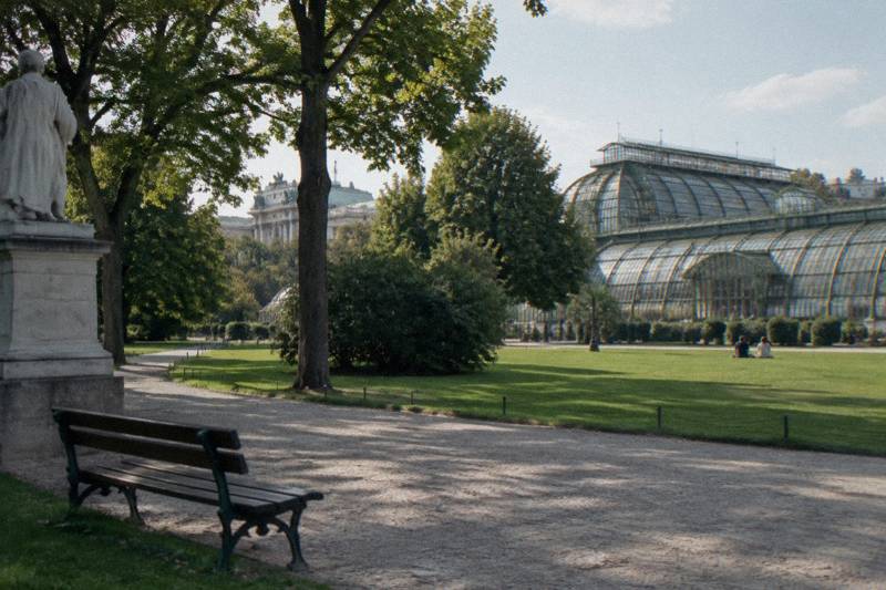 The glass-and-iron Palmenhaus beyond the lawn and old trees of the Burggarten.