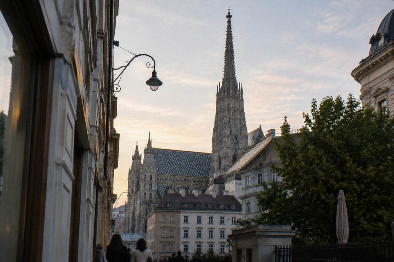 The cathedral tower rising above Vienna rooftops in early evening light, seen from a side street
