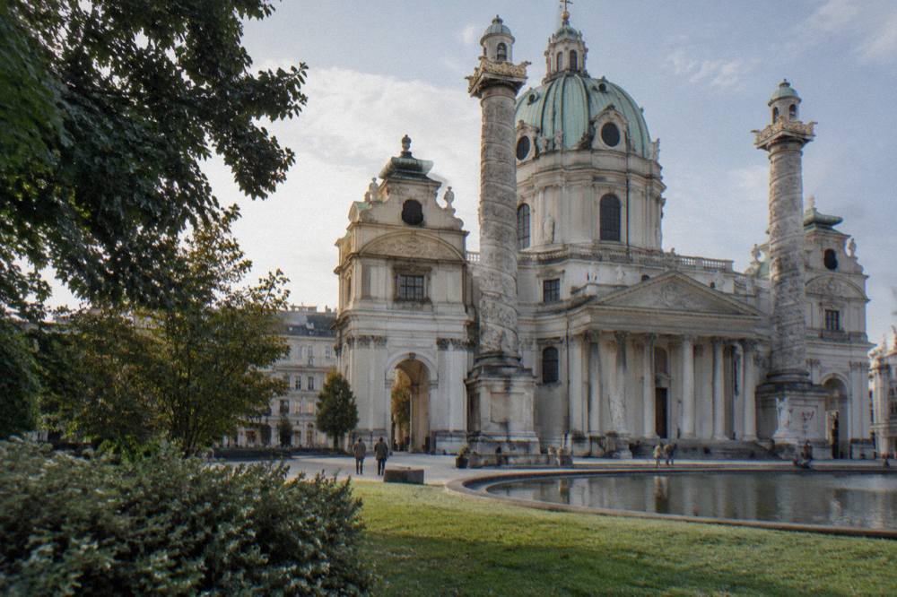 One of the two spiral relief columns of the Karlskirche rising beside the portico, seen from the lawn edge