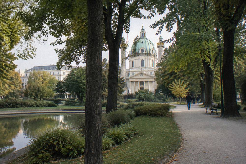 Resselpark trees and pale gravel path with the Karlskirche dome visible between the trunks