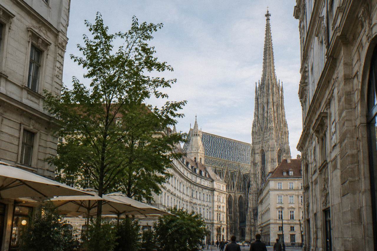 The cathedral's Gothic spire and patterned tiled roof rising above the Vienna rooftops from a nearby street