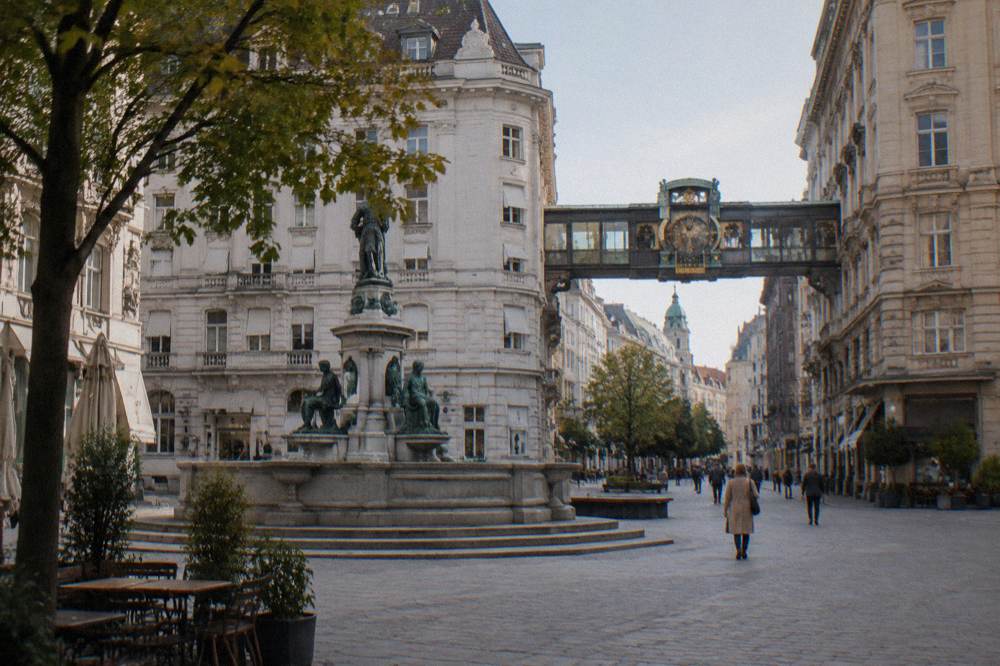 The Hoher Markt square with the Vermählungsbrunnen fountain and the glass clock bridge above the street, seen from a distance