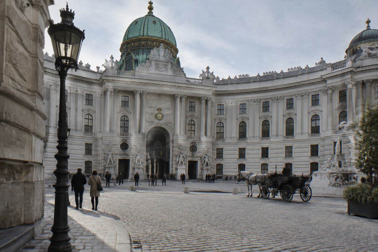 The Hofburg Michaelertor dome and curved facade seen across the open Michaelerplatz cobbles