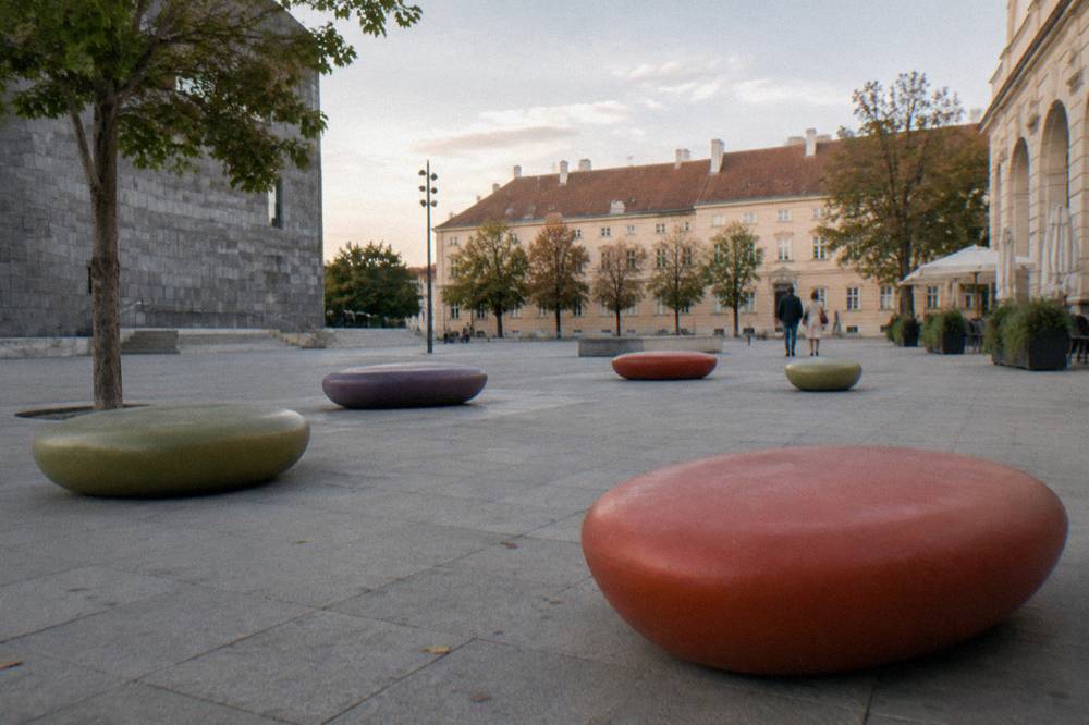 Coloured oval seating furniture scattered on the MuseumsQuartier courtyard stone, empty in soft light