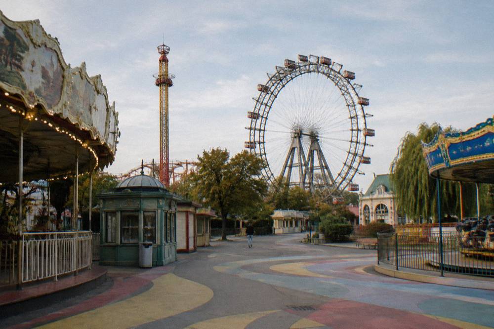 The painted walkways of the Wurstelprater fairground in the Prater with ride structures towering above, no signage readable and no crowd