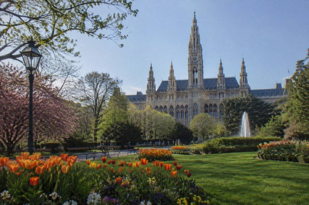 The flower beds and lawns of Rathauspark in front of the neo-Gothic Rathaus on a clear day