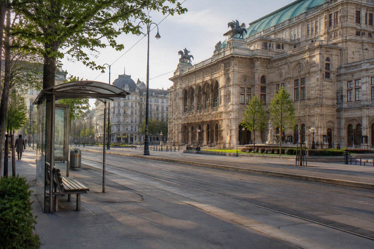 The Opernring road with the State Opera facade on one side and a tram stop with an empty bench, in morning light
