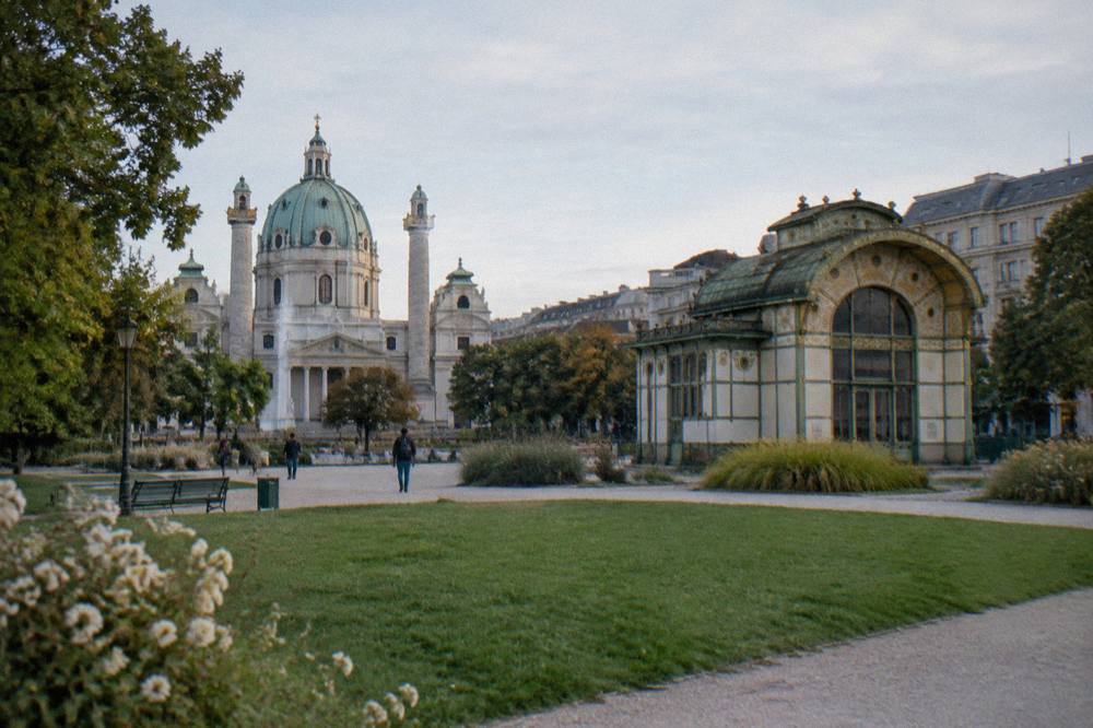 The Karlsplatz lawn with the Otto Wagner pavilion in green and gold and a few distant walkers on the gravel