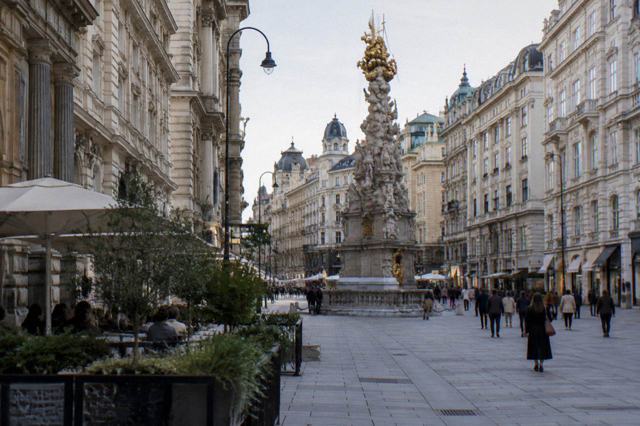 The Graben pedestrian street with its ornate Plague Column and pale historic facades on a busy-looking afternoon, people distant