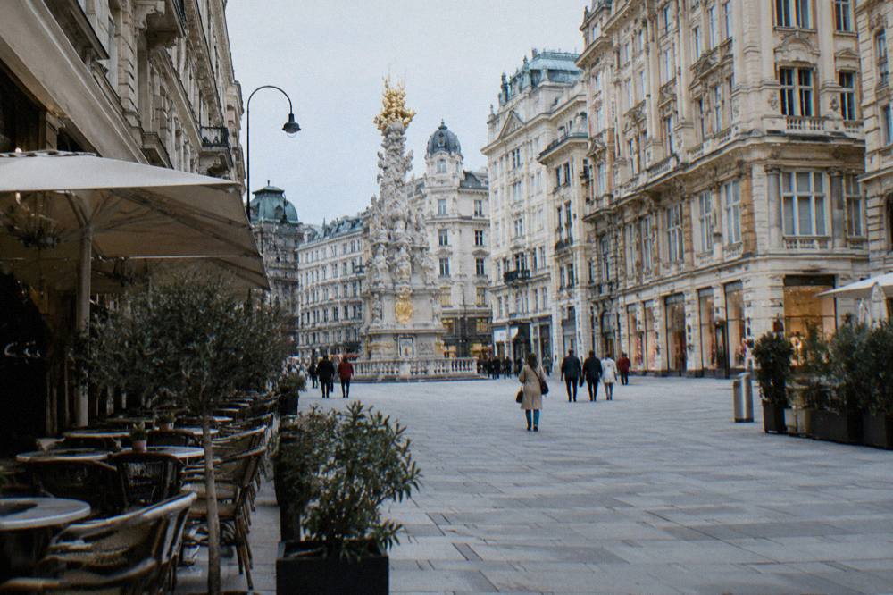 A pedestrian shopping street in the old town with historic facades and cafe tables outside, people distant
