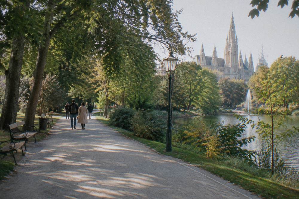 A tree-lined path in the Stadtpark with a broad gravel walking surface and sunlight through leaves