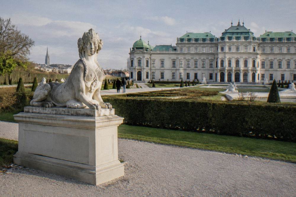 The Lower Belvedere's low garden front with a stone sphinx statue on a plinth and a gravel path in the foreground