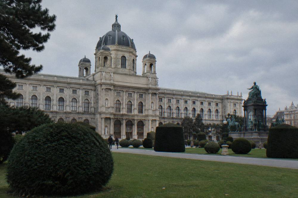 The Naturhistorisches Museum facade across the lawn of Maria-Theresien-Platz with its large central dome and rows of stone statues