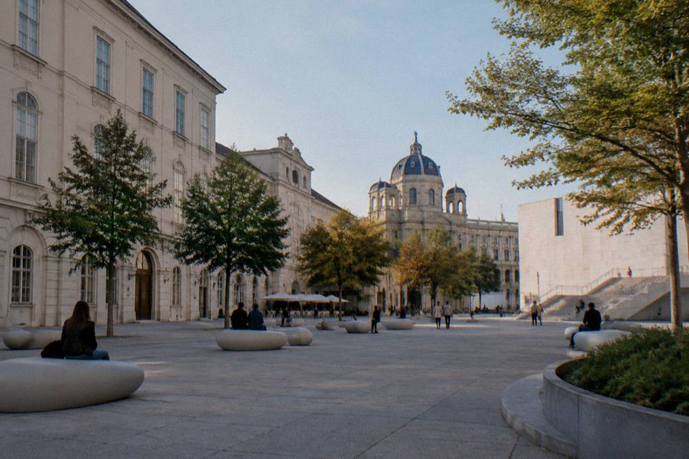 The MuseumsQuartier courtyard with its pale stone buildings, scattered oval seating furniture and a clear sky above