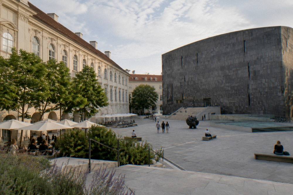 The sunken MuseumsQuartier courtyard with the long dark basalt museum block opposite the pale Baroque facade of the old stables