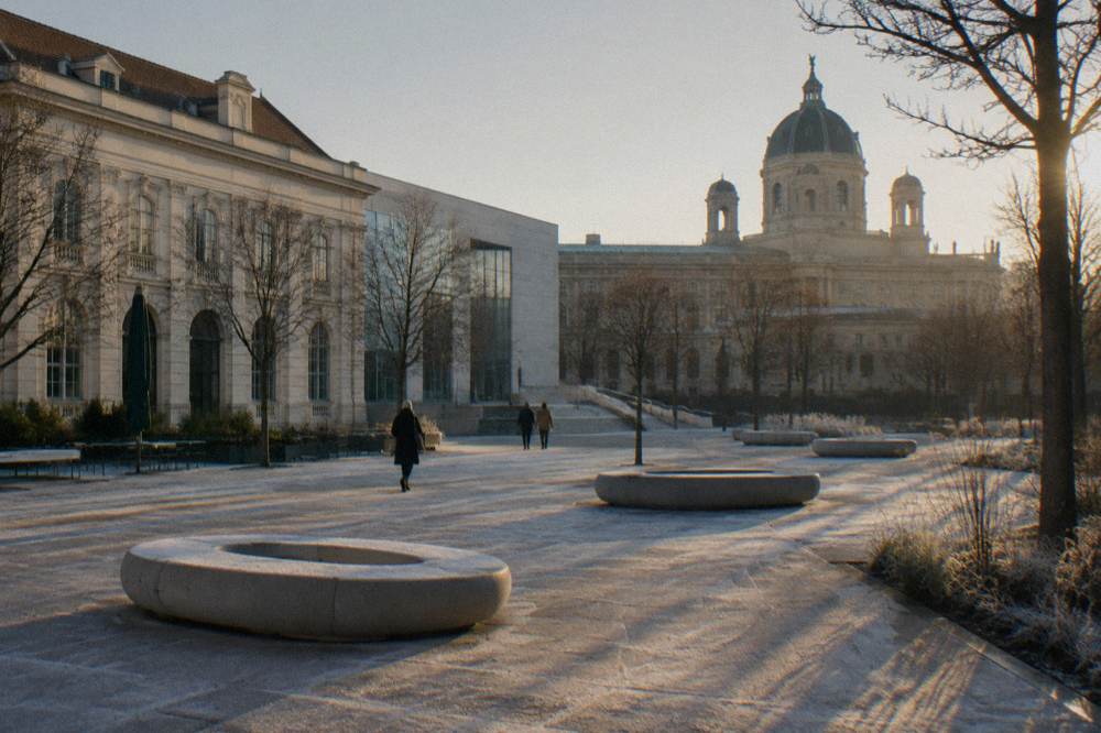 A frosted MuseumsQuartier courtyard in low winter sun with empty oval benches and long shadows