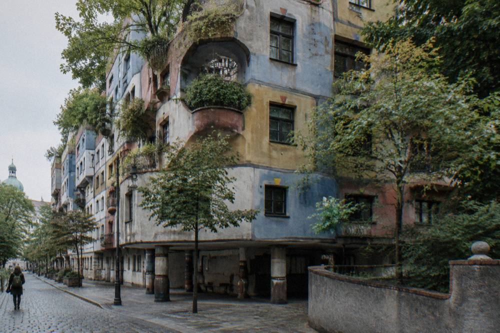 The wavy coloured facade of the Hundertwasserhaus with tree-planted balconies seen from the quiet street corner