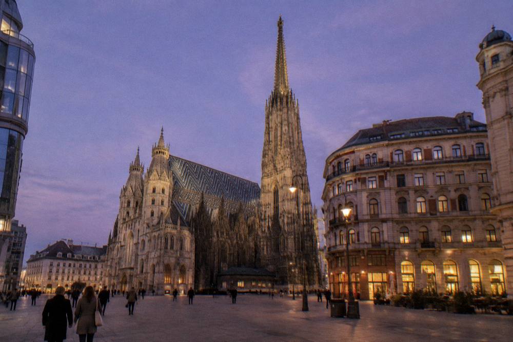 Stephansplatz at dusk with the cathedral spire lit against a violet sky and a few distant visitors crossing the paving