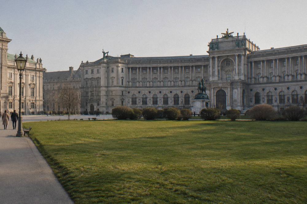The wide open lawn of Heldenplatz with the curved Neue Burg wing beyond, empty in morning light