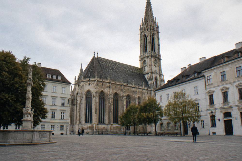 The Minoritenplatz square with the Gothic Minorite Church facade and tower rising behind the plain cobbles