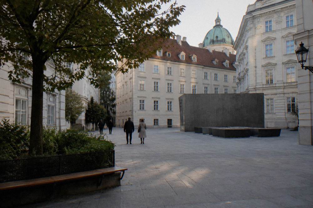The Judenplatz square with plain pale facades and a few distant people seen from behind in the afternoon