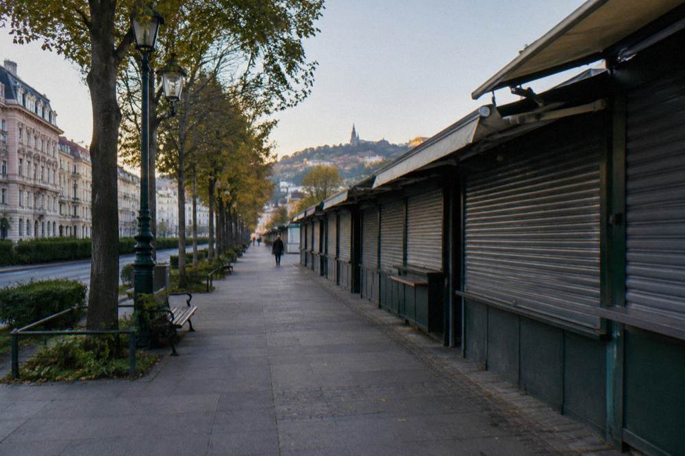 The Linke Wienzeile market walkway in early morning light with shutters still down on the stalls and a quiet pavement