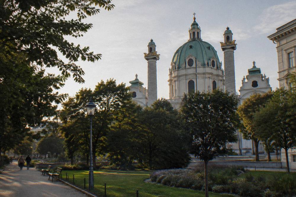 The dome and twin columns of the Karlskirche rising behind the Resselpark trees seen from a few streets away