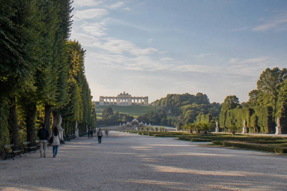 A wide tree-lined garden avenue in the Schönbrunn park with the Gloriette small at the far end