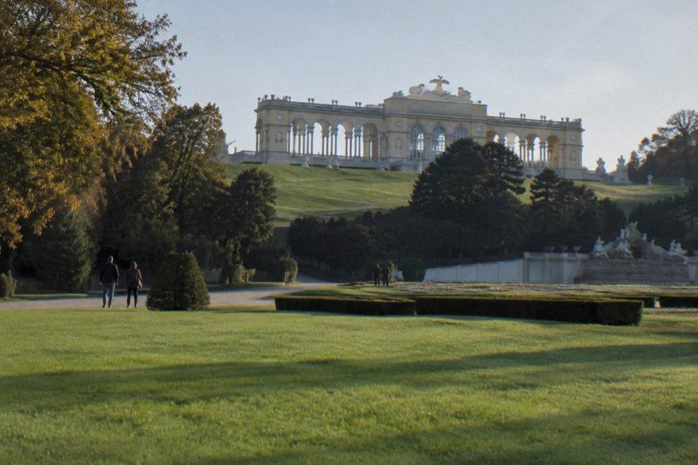 The colonnaded Gloriette on its hilltop above formal hedges, photographed from the lawn below in morning light