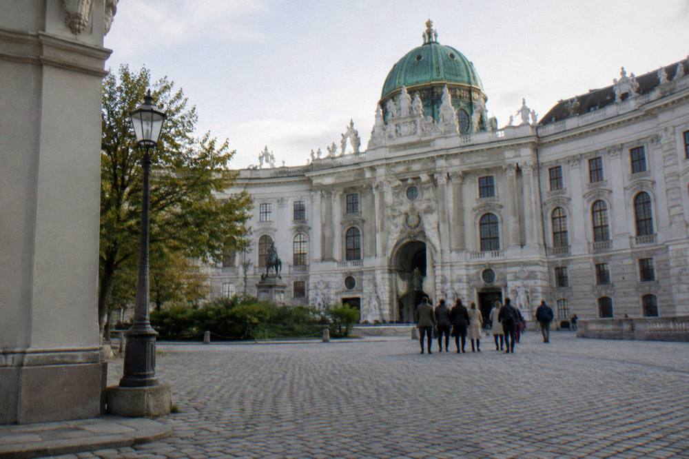 Josefsplatz cobbles and the pale Baroque library facade with a group of distant visitors seen from behind