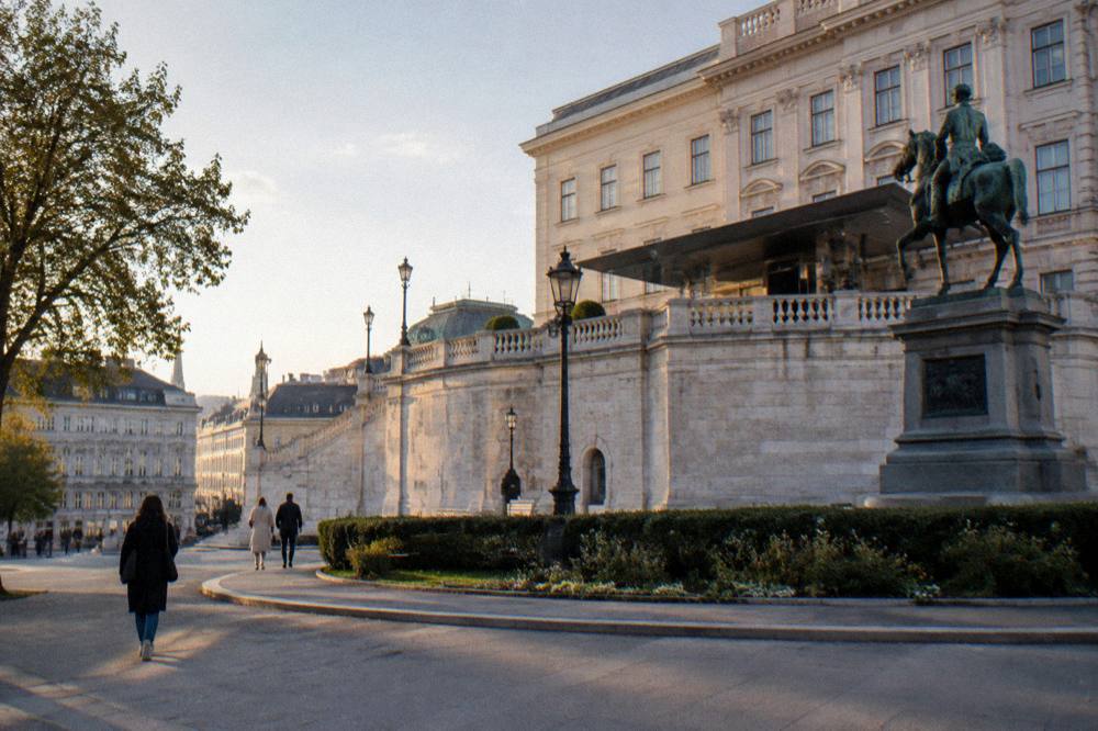 The Albertina's pale classical facade and its high bastion terrace wall seen from the square in late afternoon light