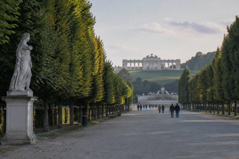 A tree-lined avenue in the Schönbrunn park with the Gloriette distant at the end in soft light
