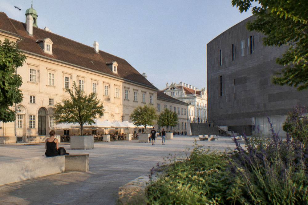 The MuseumsQuartier courtyard where the old Baroque stables meet the dark modern museum blocks, under clear daylight