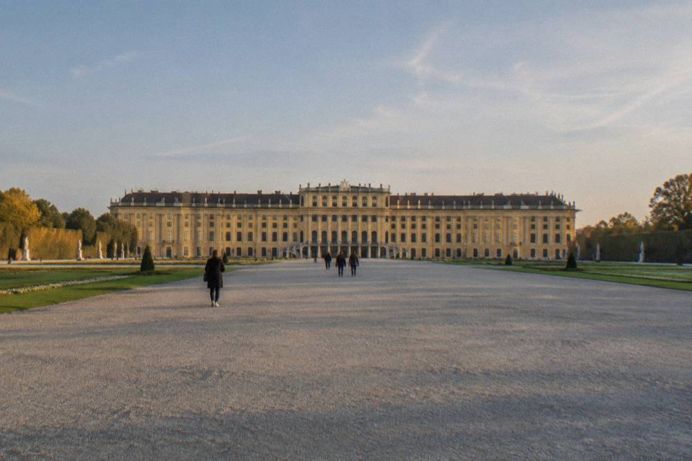 The ochre yellow palace facade of Schönbrunn from the far end of the empty forecourt in early morning light