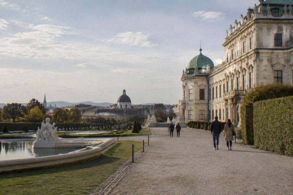 A gravel walk beside a Baroque Belvedere palace wing with trimmed hedges and open sky