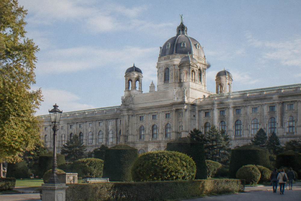 The Kunsthistorisches Museum dome and rooftop statues against a soft blue sky seen from across the road